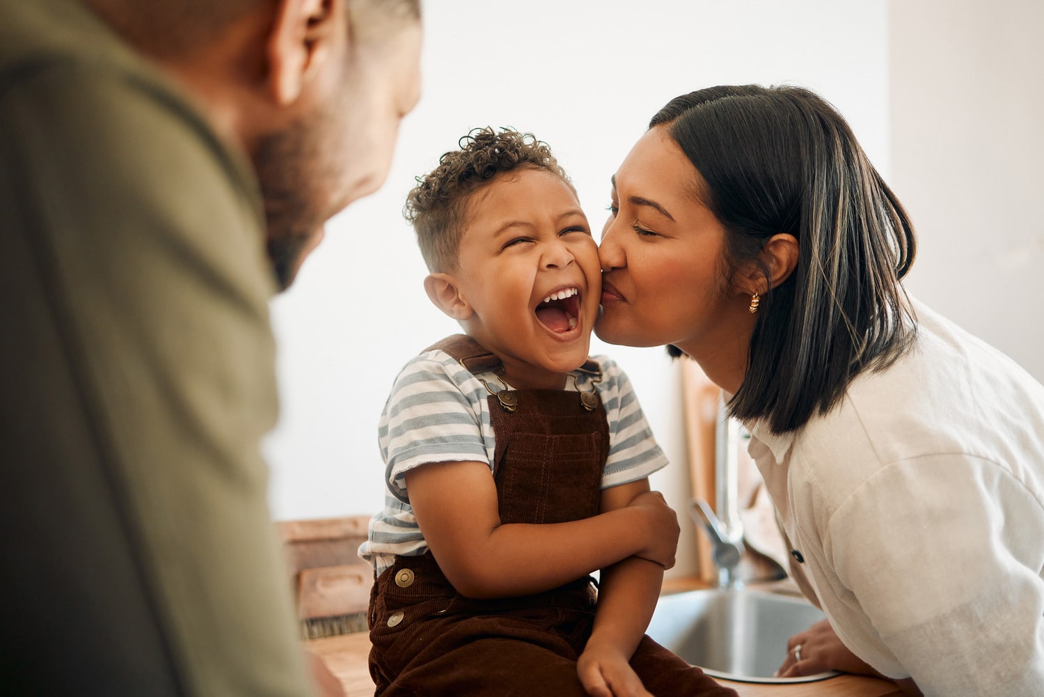 Boy back home after a general anesthesia dental appointment laughing as his mom gives him a kiss on the cheek in Brooklyn NY